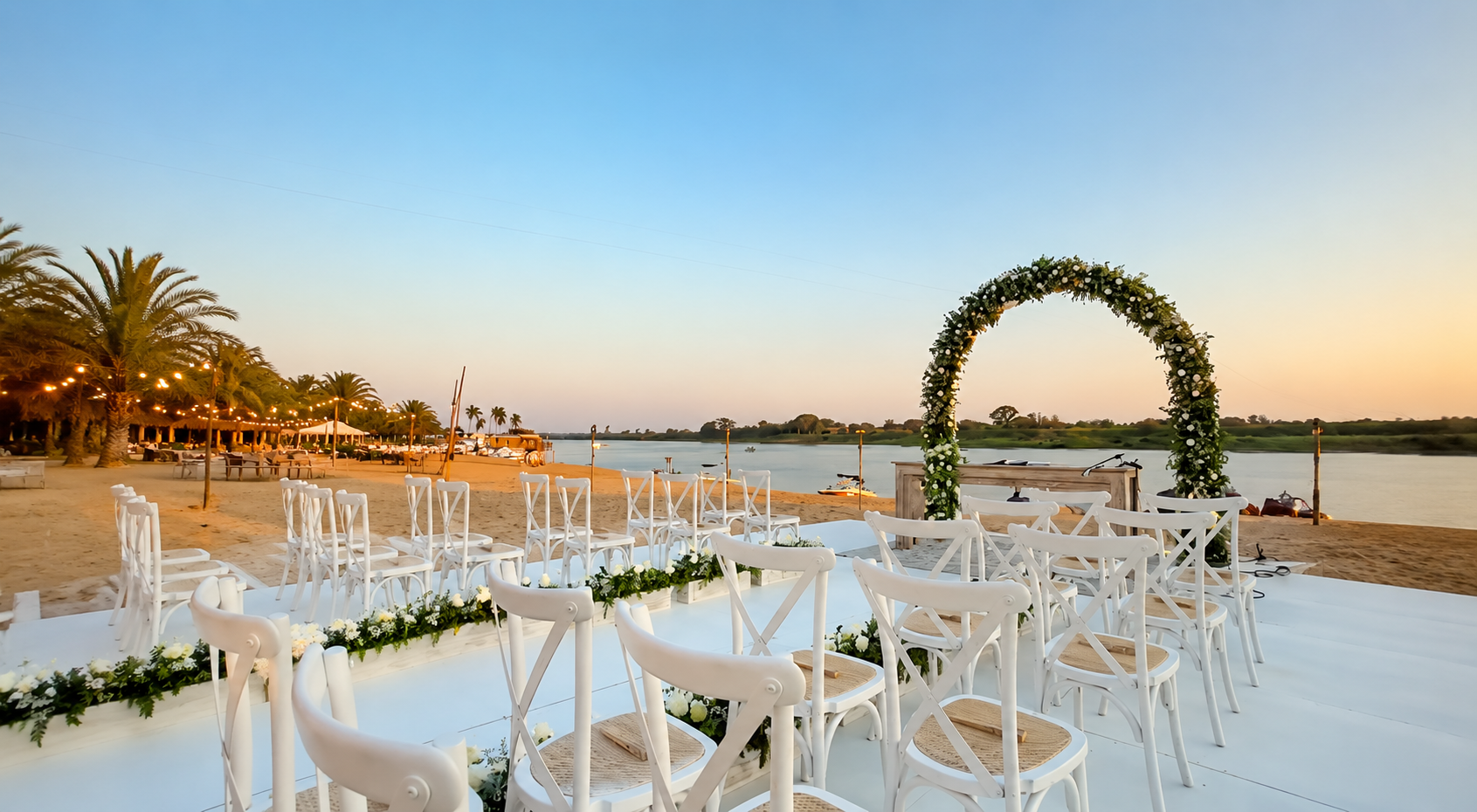 Ceremonia de bodas montada en la playa con arco floral, sillas blancas y vista al río Paraguay al atardecer